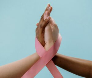 Pink Ribbon Schleife an Frauenhänden als Symbol für Bewusstsein und Solidarität mit an Brustkrebs Erkrankten.